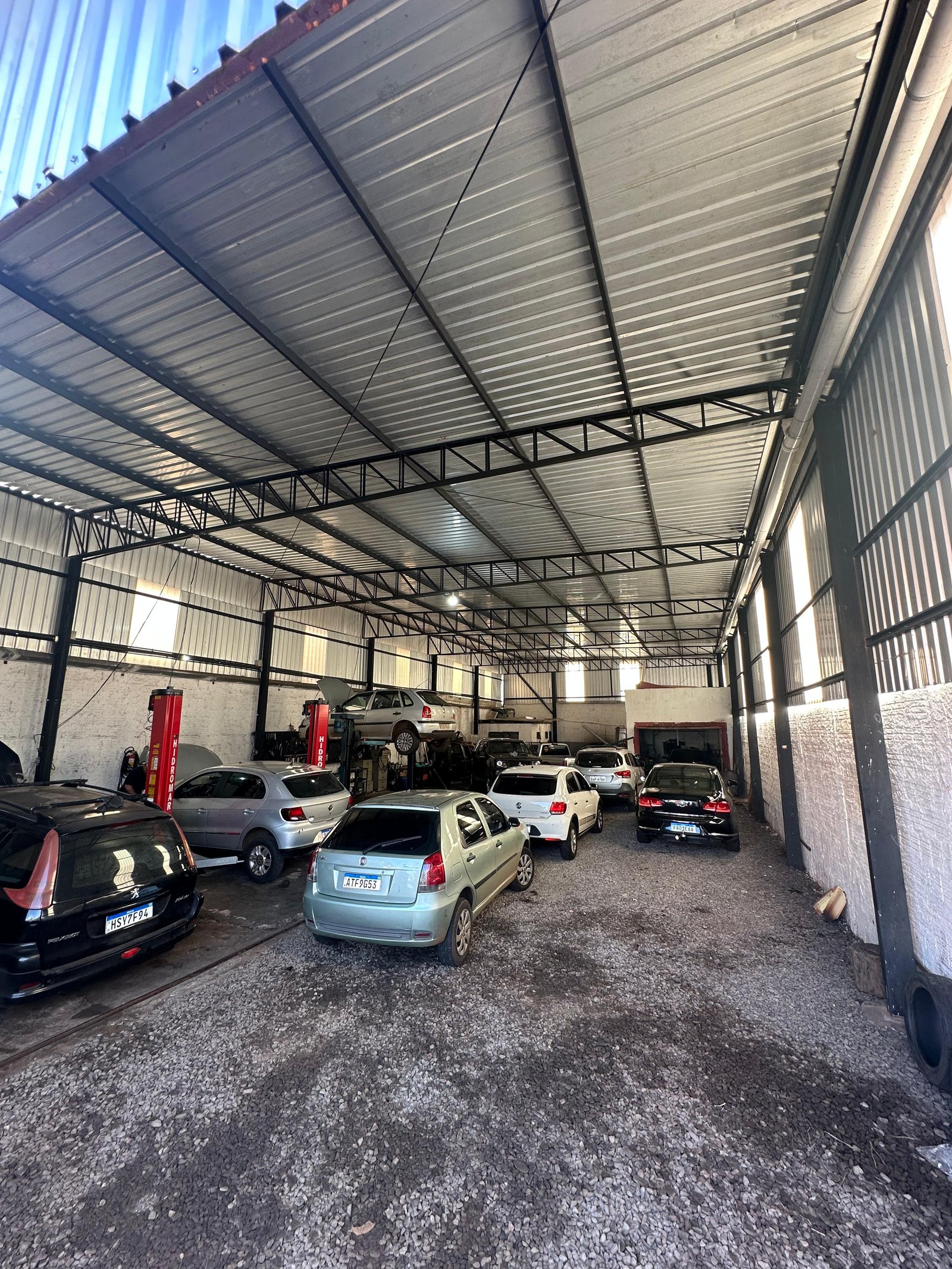 Interior do galpão coberto da Atir com elevadores vermelhos e vários veículos